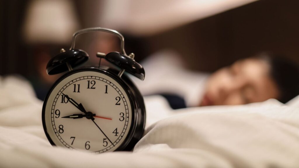 Selective focus of a clock showing 9 PM with a boy sleeping on bed